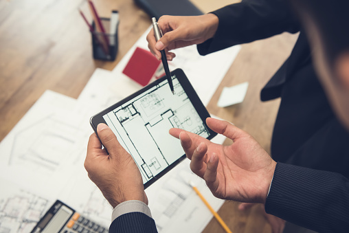 Real estate agent with client or architect team discussing a housing model and its blueprints digitally using a tablet computer